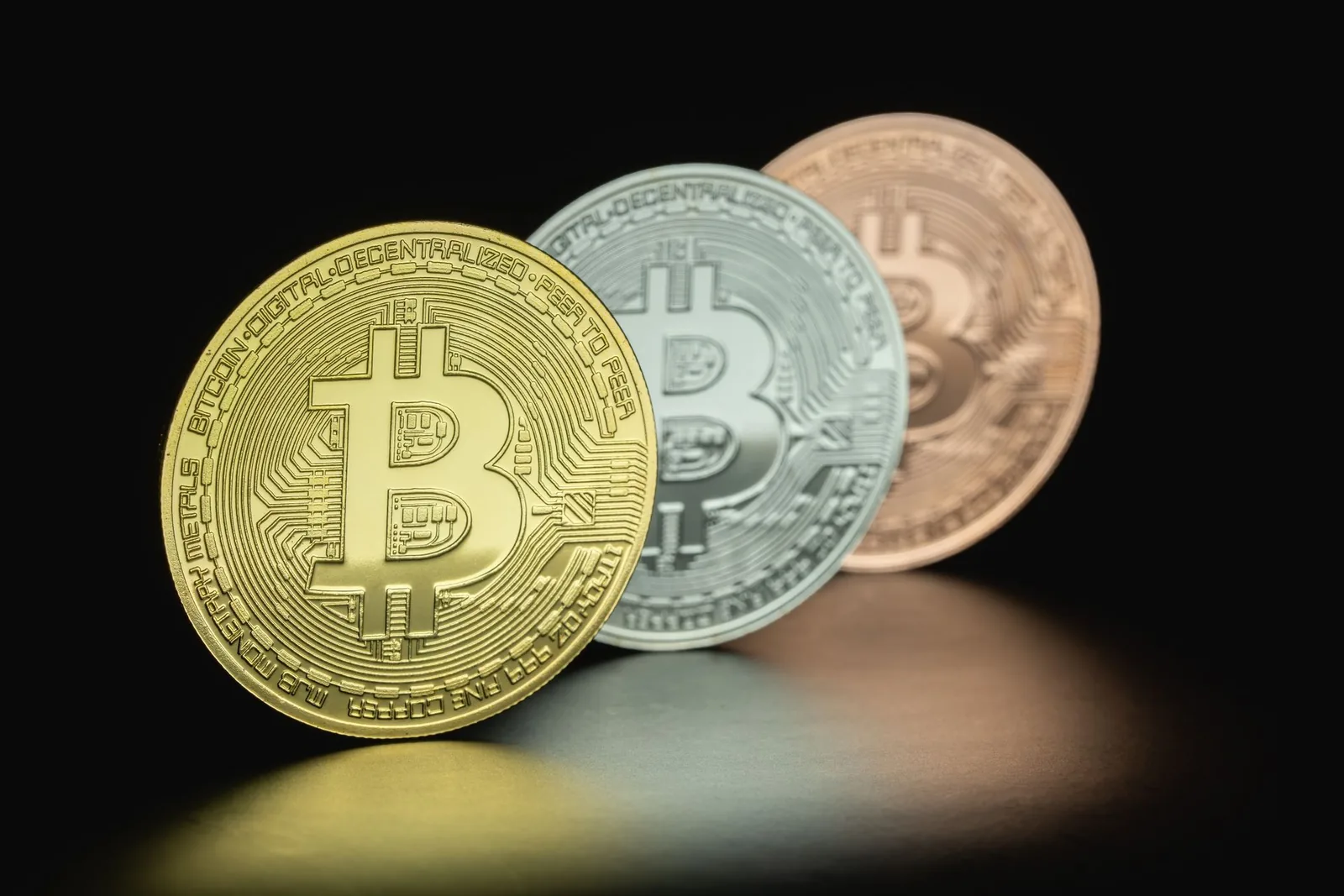 Kolme erivärisiä bitcoin-kolikkoa mustaa taustaa vasten