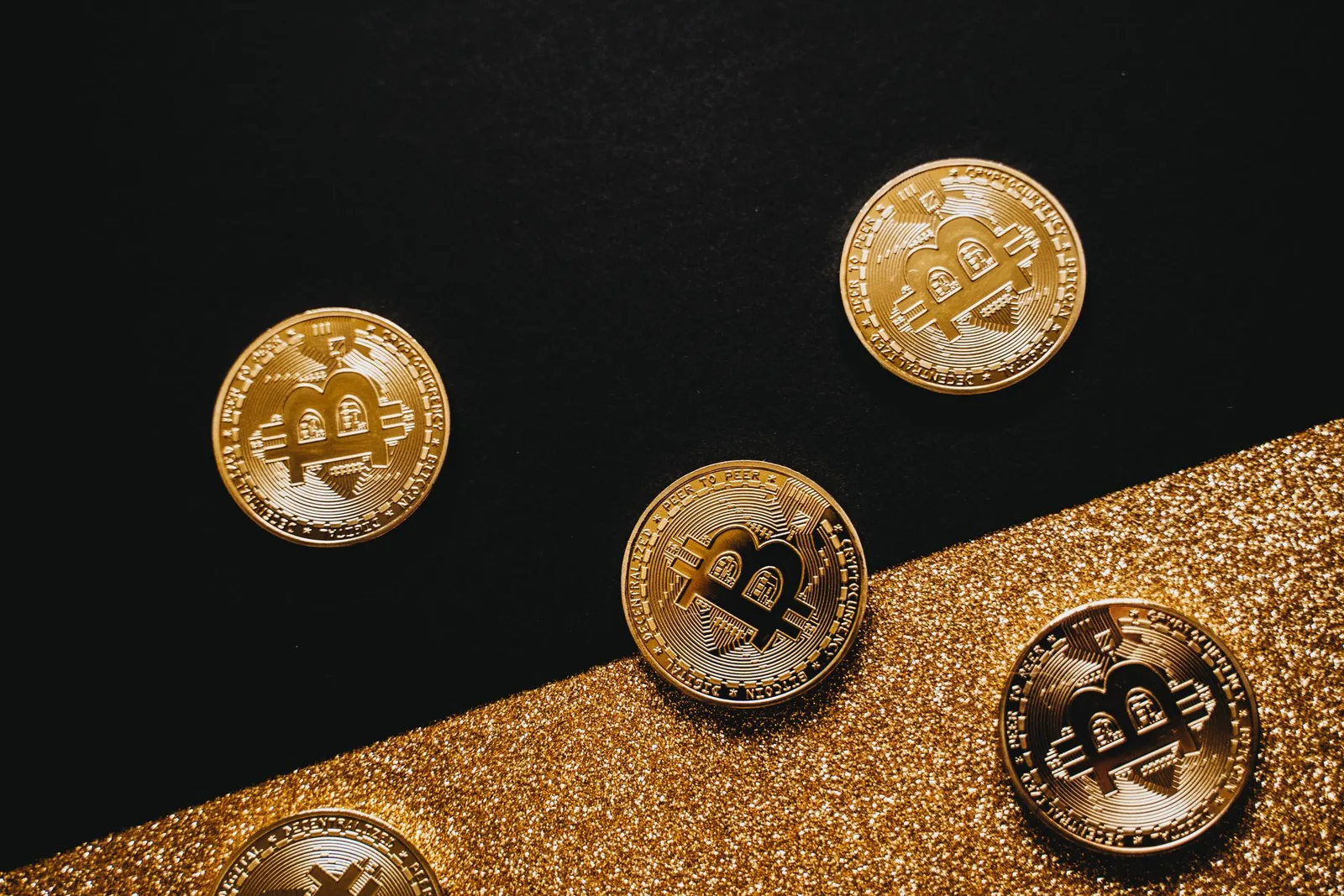 Neljä bitcoin-kolikkoa mustalla ja kultaisella pinnalla
