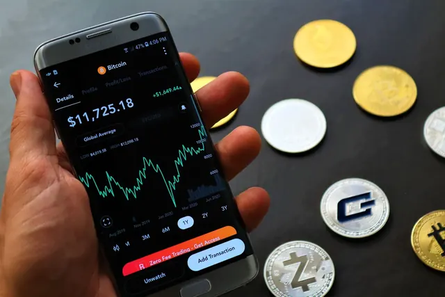 Kädessä älypuhelin, jonka ruudulla on kurssikäyrä, ympärillä kolikoita